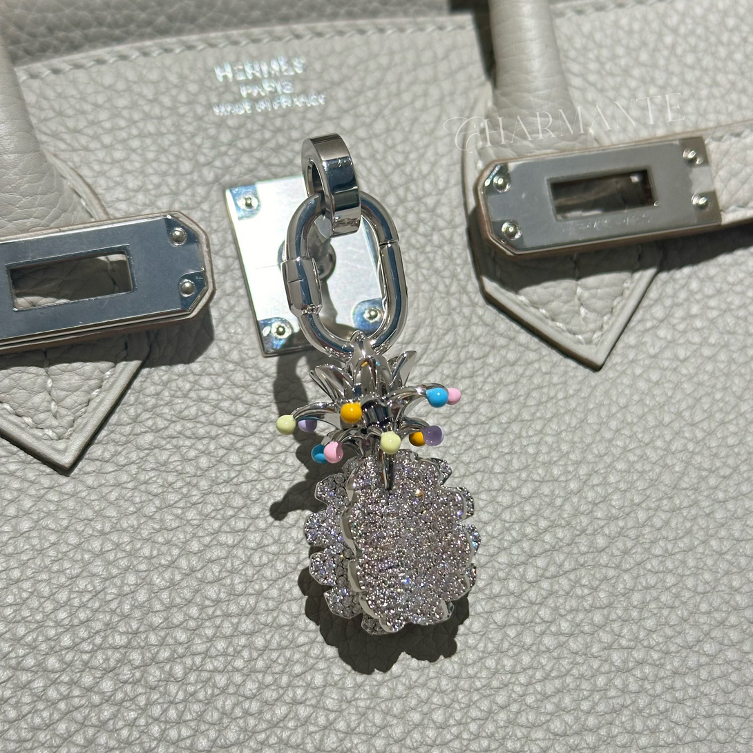 Silver pineapple bag charm with colorful leave beads on a gray birkin 25