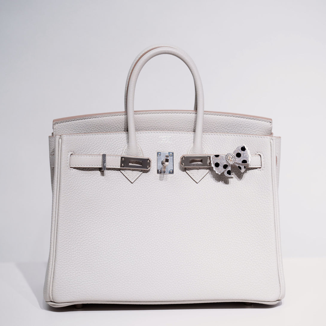 White birkin handbag with silver hardware and a decorative bow on a light gray background