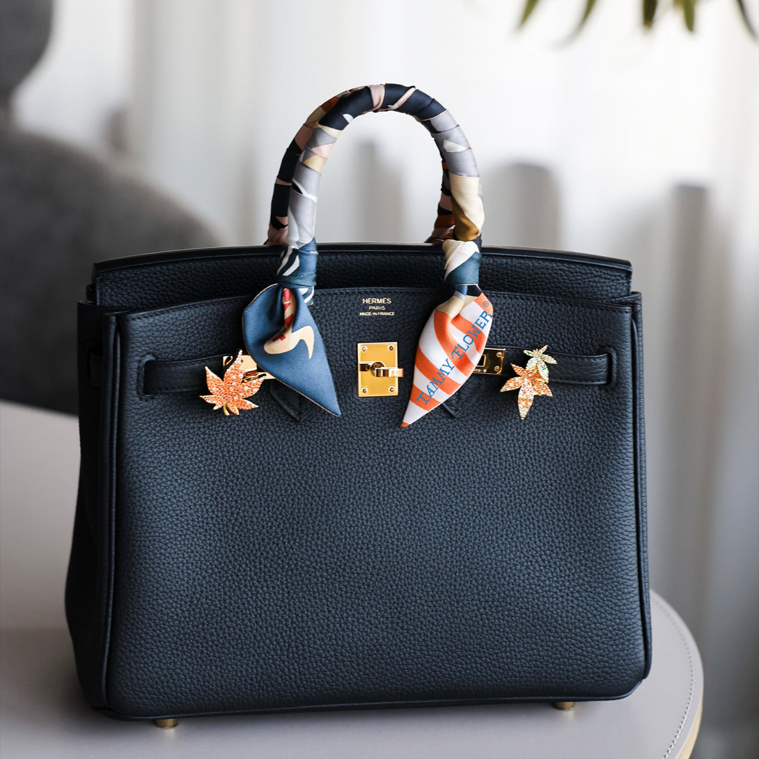 Black birkin handbag with decorative fall autumn fashion maple leaf on a light surface