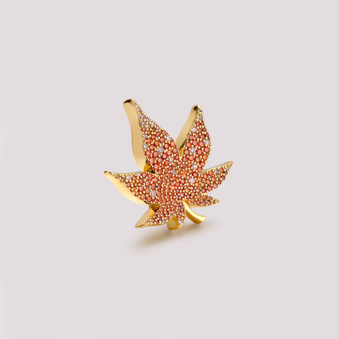 Gold and red leaf-shaped bag charm on a light gray background