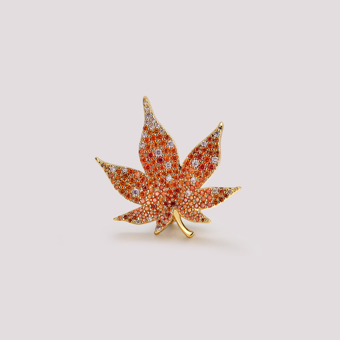 Maple leaf bag charm with red gemstones and gold accents on a light gray background