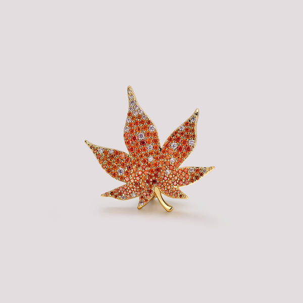 Maple leaf bag charm with red gemstones and gold accents on a light gray background