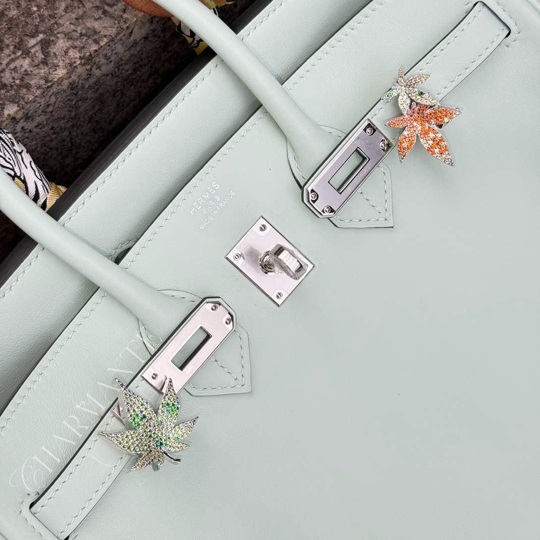 Light green vert birkin handbag with decorative fall autumn maple leaf pin on a textured surface